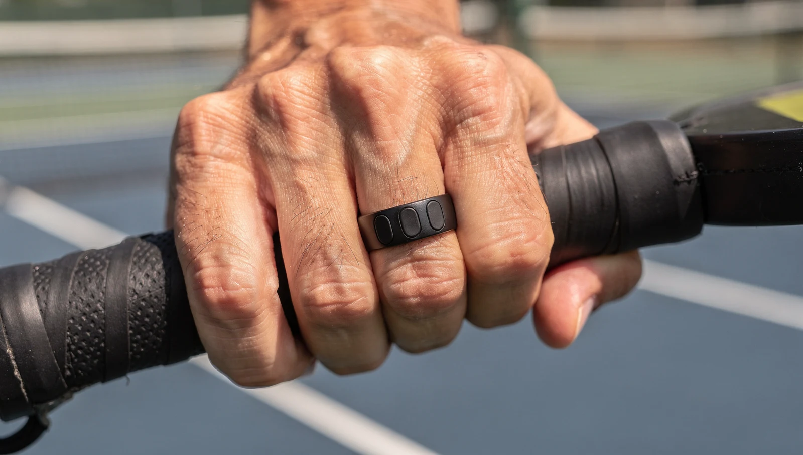 Close-up of a hand wearing the ScoreTap Ring while gripping a pickleball paddle mid-match